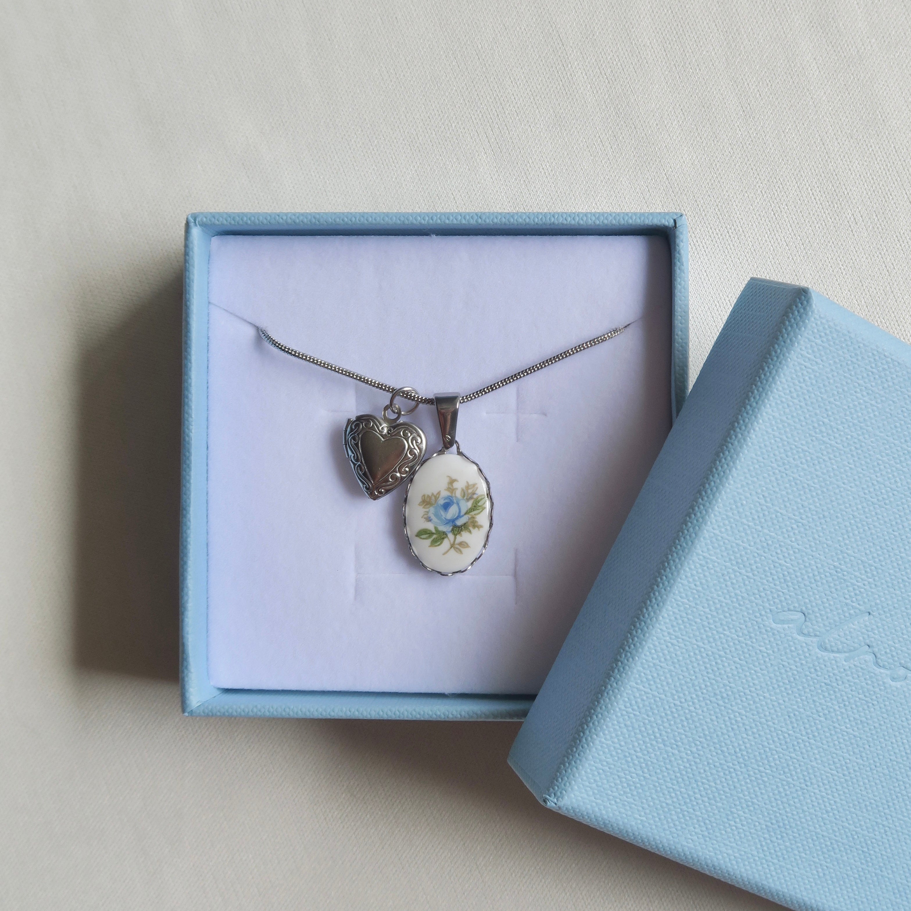 Necklace with heart-shaped pendant in a light blue jewelry box on a beige background