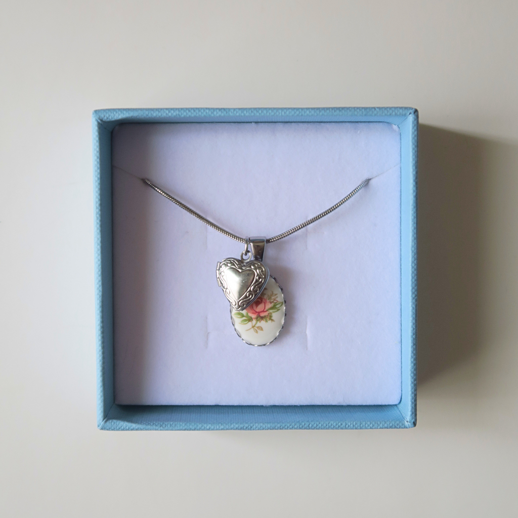 Necklace with a floral pendant and a silver heart in a blue box on a light beige background