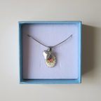 Necklace with a floral pendant and a silver heart in a blue box on a light beige background