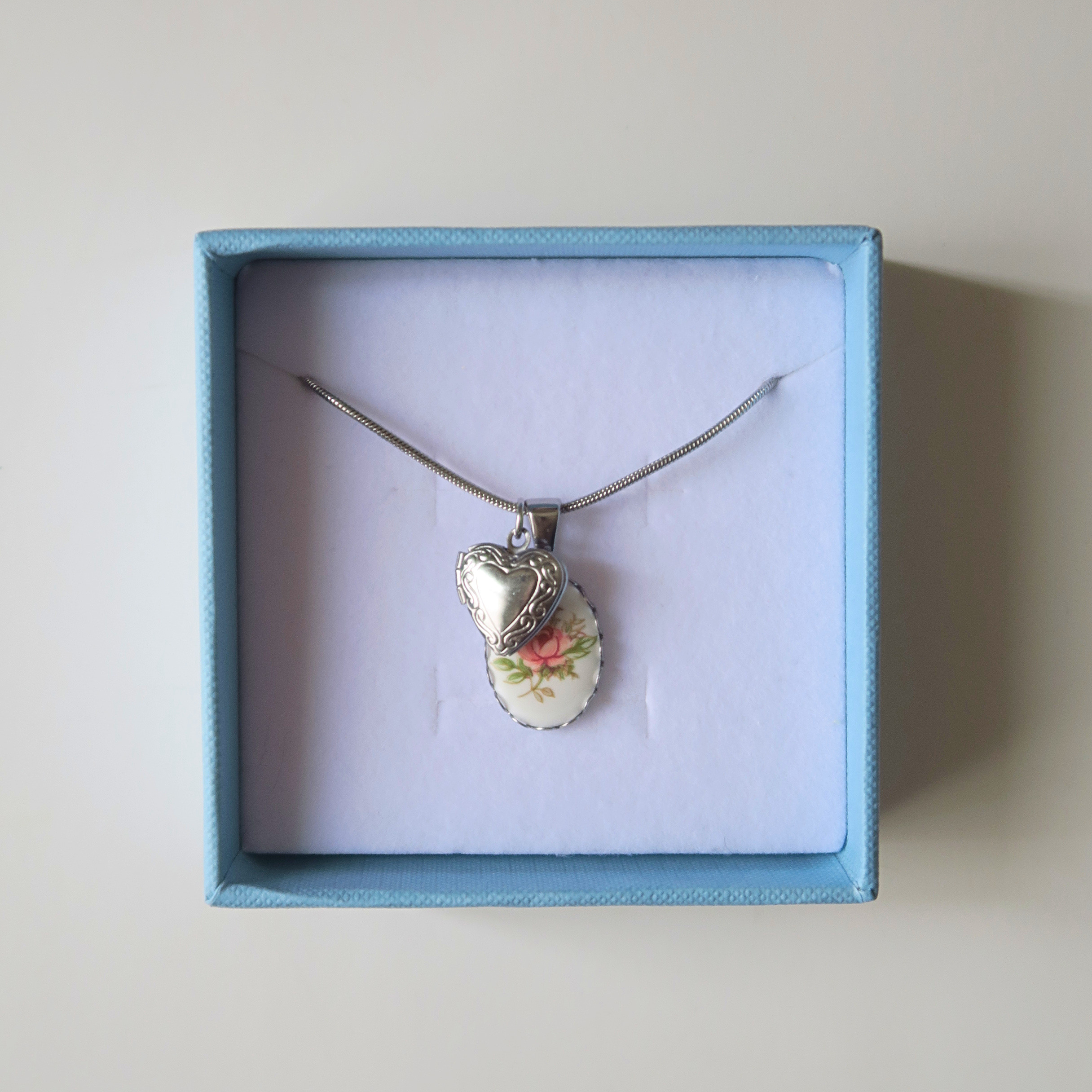 Necklace with a floral pendant and a silver heart in a blue box on a light beige background