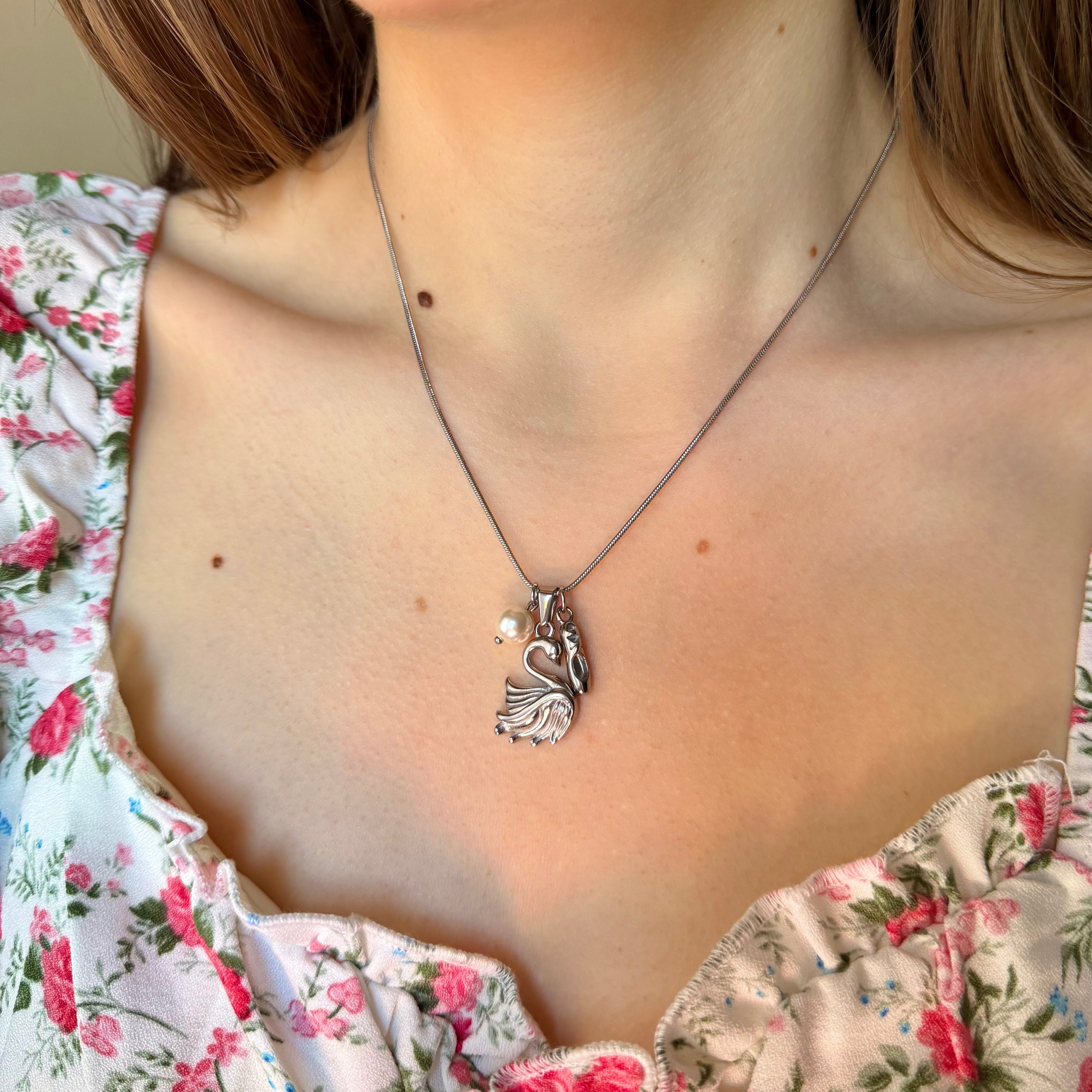 Necklace with a swan pendant, pearl, and ballet slipper charm worn by a person in a floral top