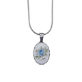 An oval pendant necklace featuring a white cabochon with a delicate blue rose and green leaves, set in a silver bezel on a silver snake chain.