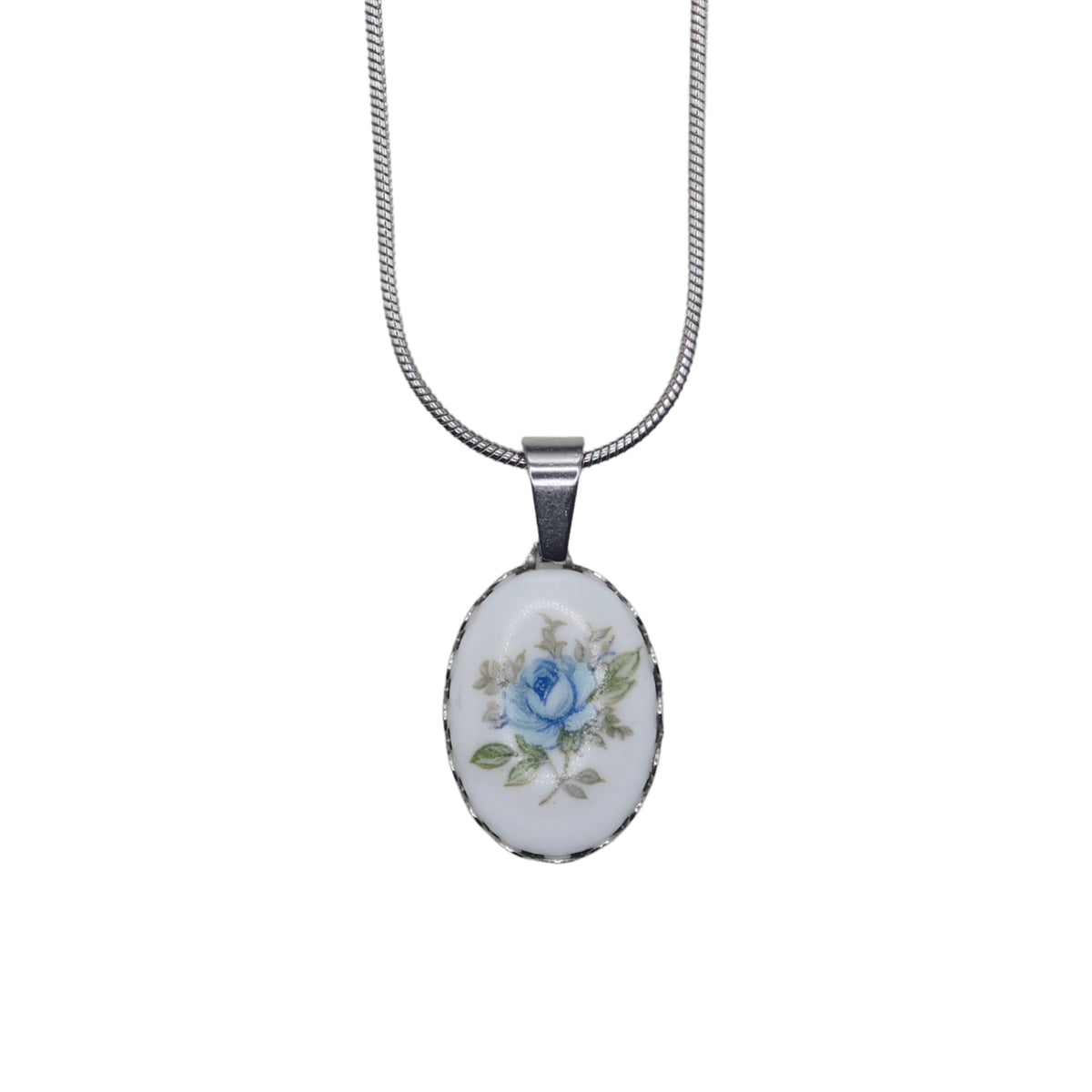 An oval pendant necklace featuring a white cabochon with a delicate blue rose and green leaves, set in a silver bezel on a silver snake chain.